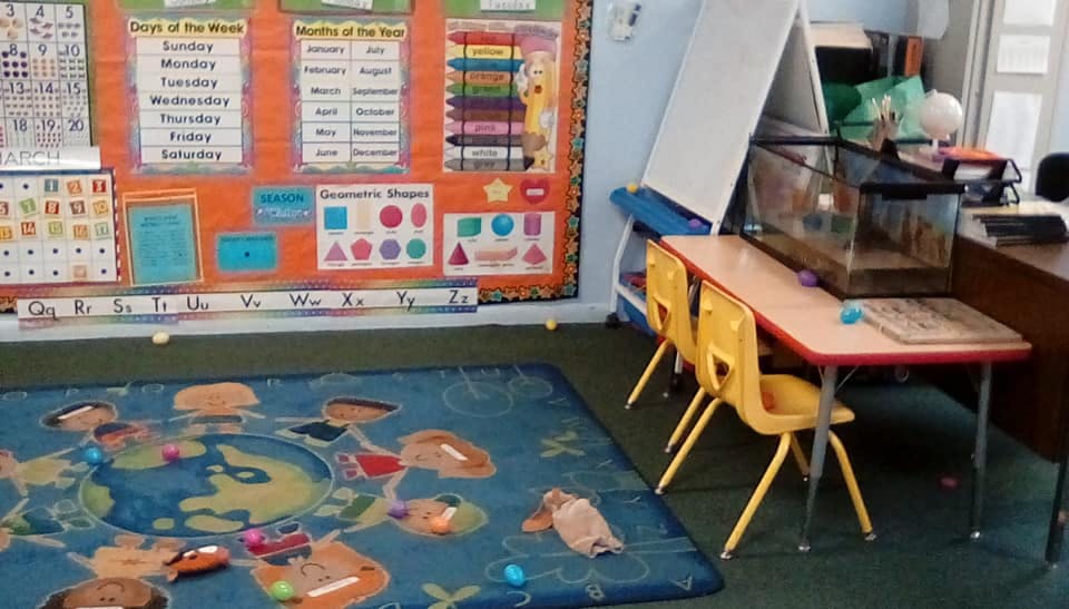 Classroom with a world map rug, bulletin board, and small table with chairs