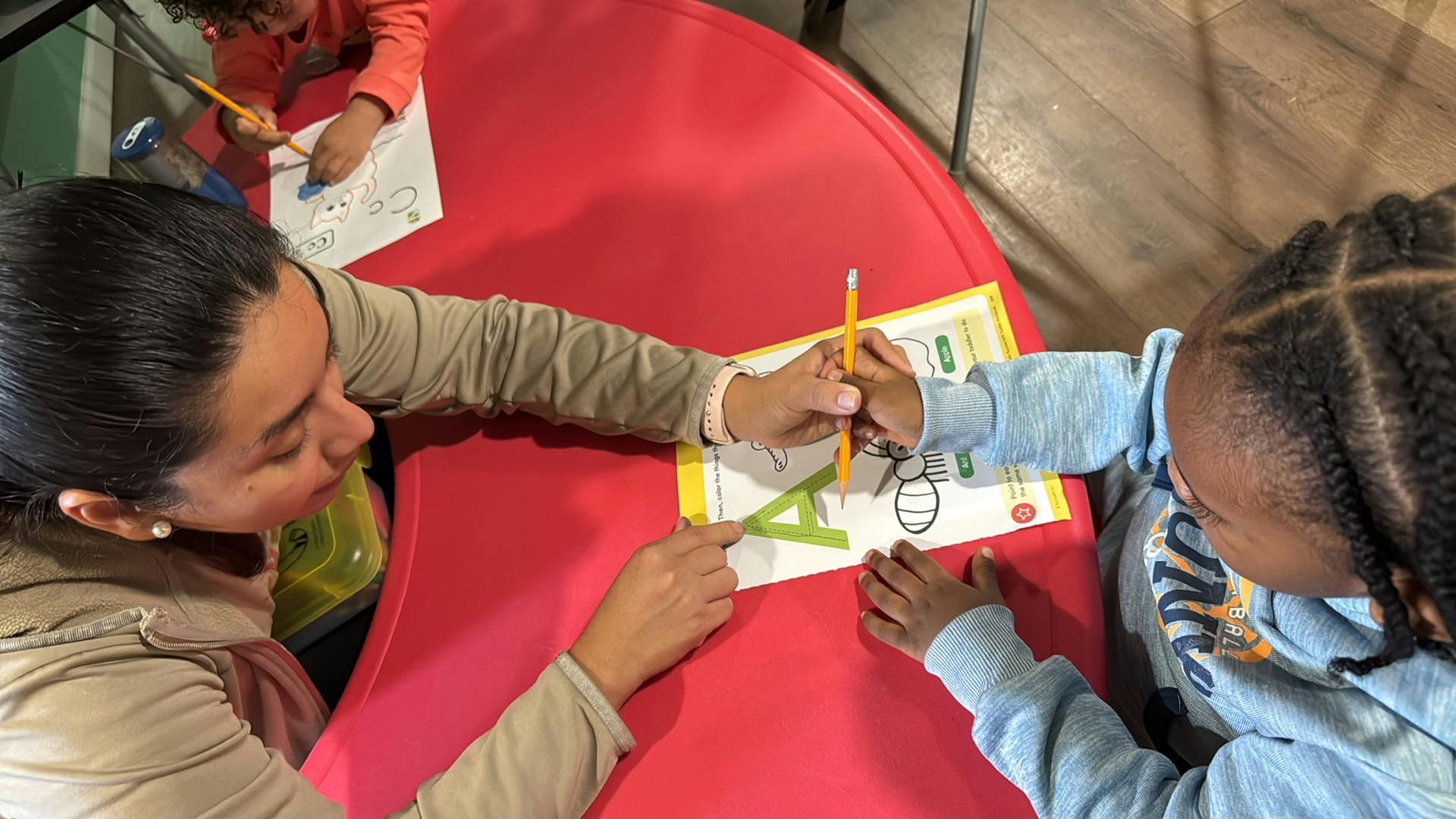 Adult guiding a child hand while writing the letter A on a worksheet