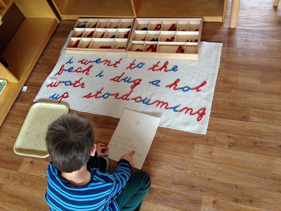 Child sitting on floor looking at paper with alphabet boxes and word mat