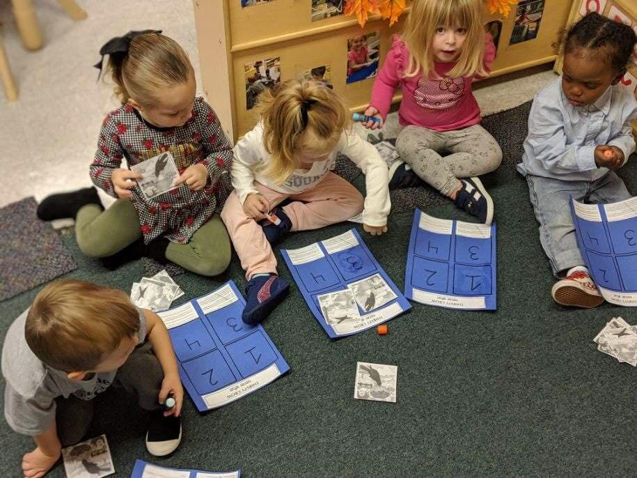 Four children sitting on the floor playing a game with cards and blue mats