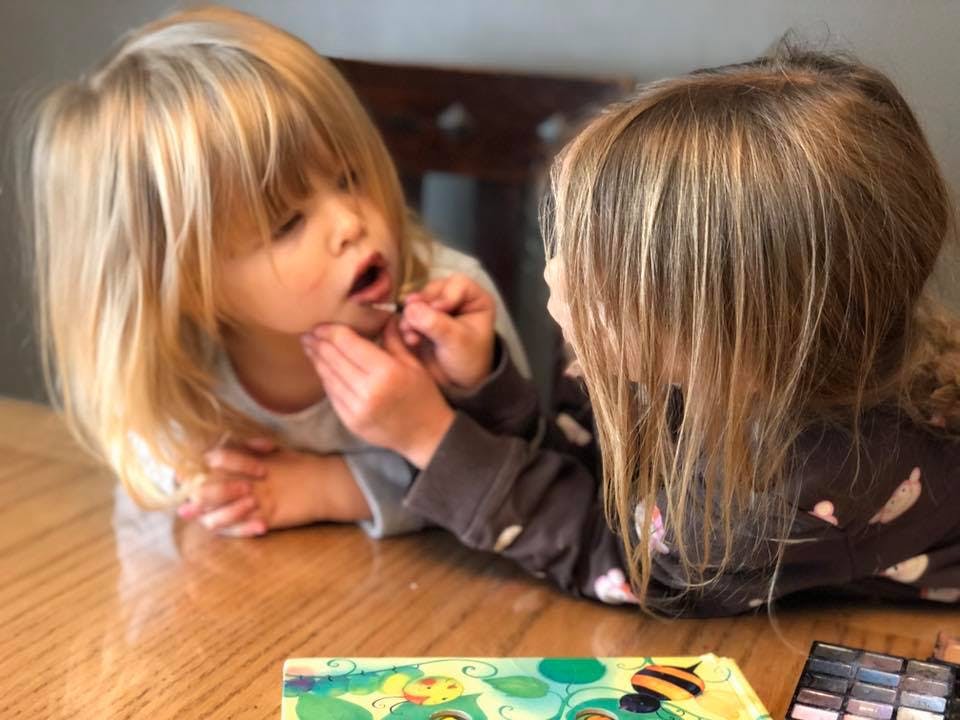 Child applying makeup to another child's face