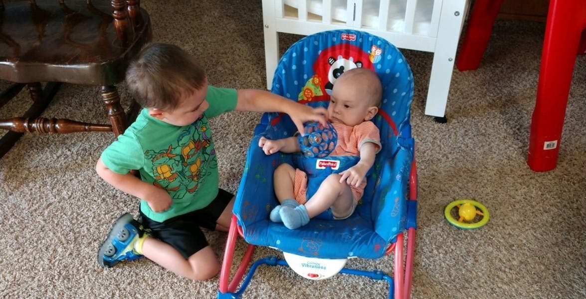 Child kneeling next to baby in a bouncer seat