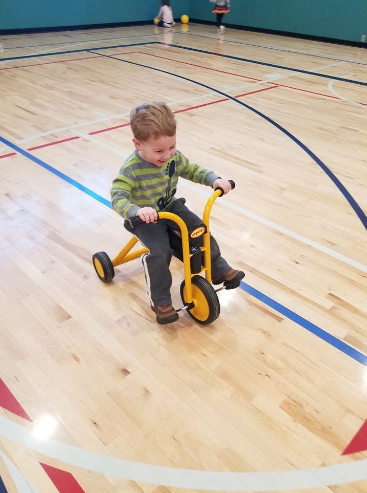 Child riding a yellow tricycle on a gym floor