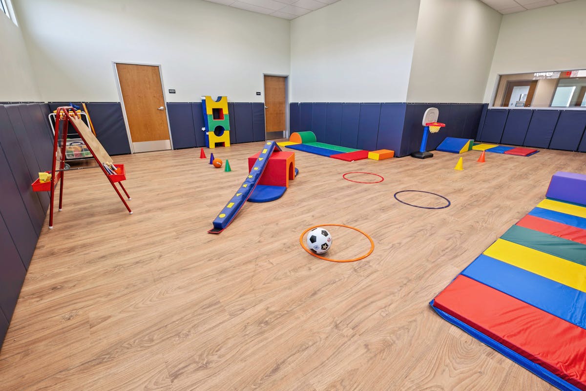 Indoor playroom with various colorful soft play equipment, mats, and a soccer ball