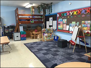 Empty classroom with a bunk bed, rug, and bulletin board