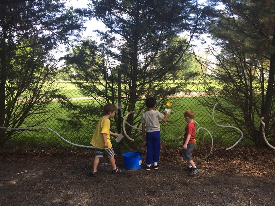 Three children playing with water and tubes outdoors