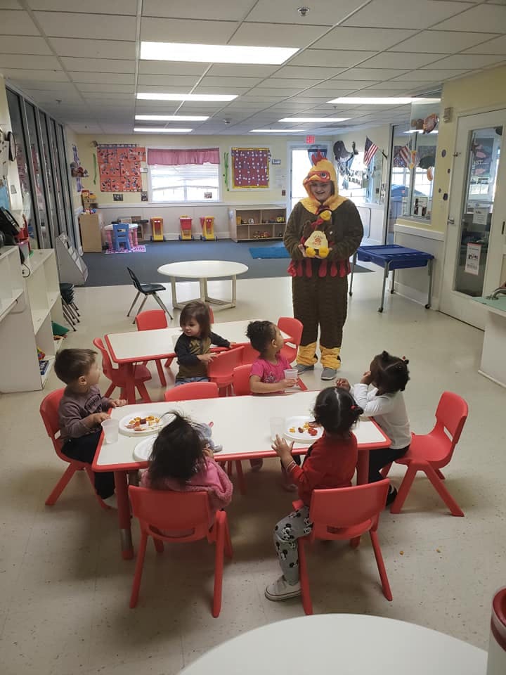Person in costume standing near children seated at tables in a classroom