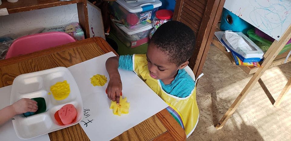 Child painting with sponges and yellow paint