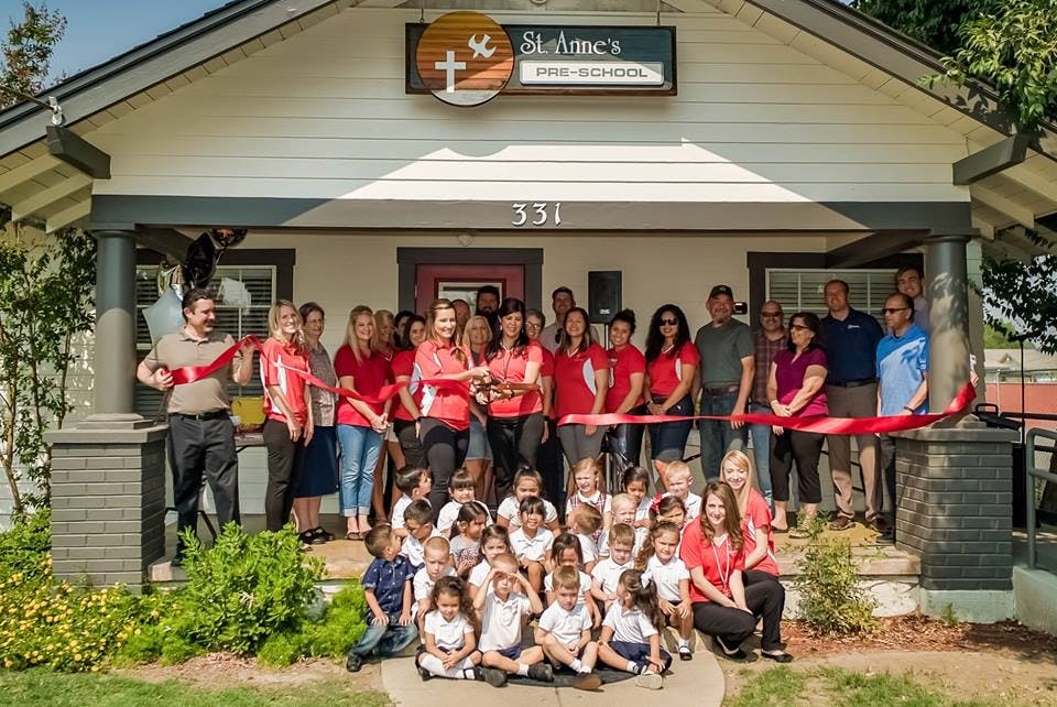 Adults and children gathered in front of a building with a red ribbon