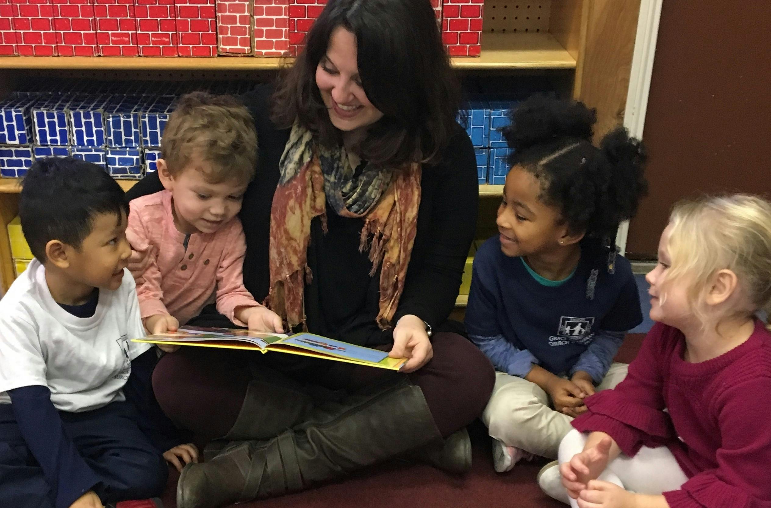 Person reading a book to four children in a classroom