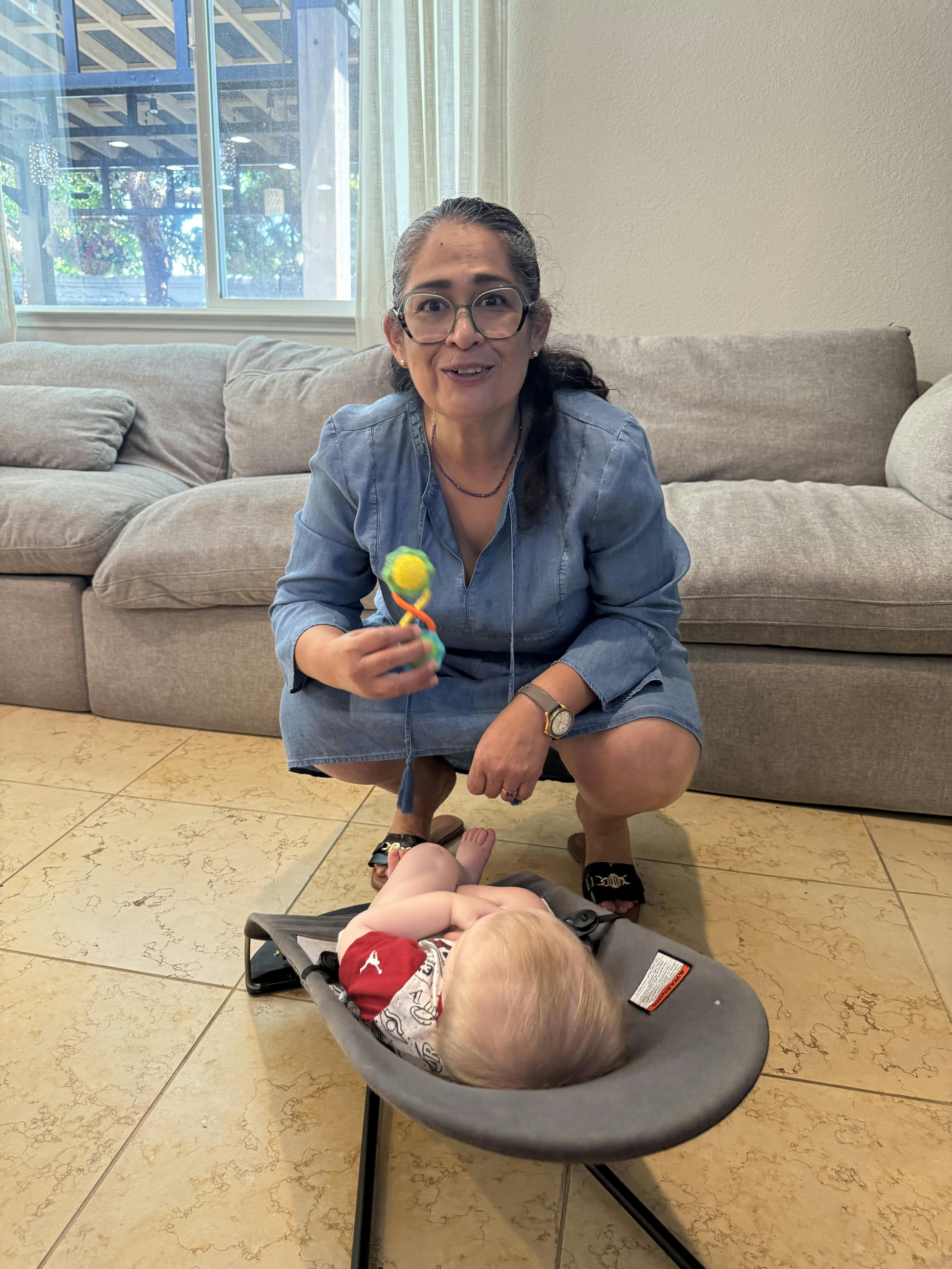 Person squatting and holding a rattle for a child in a bouncer seat