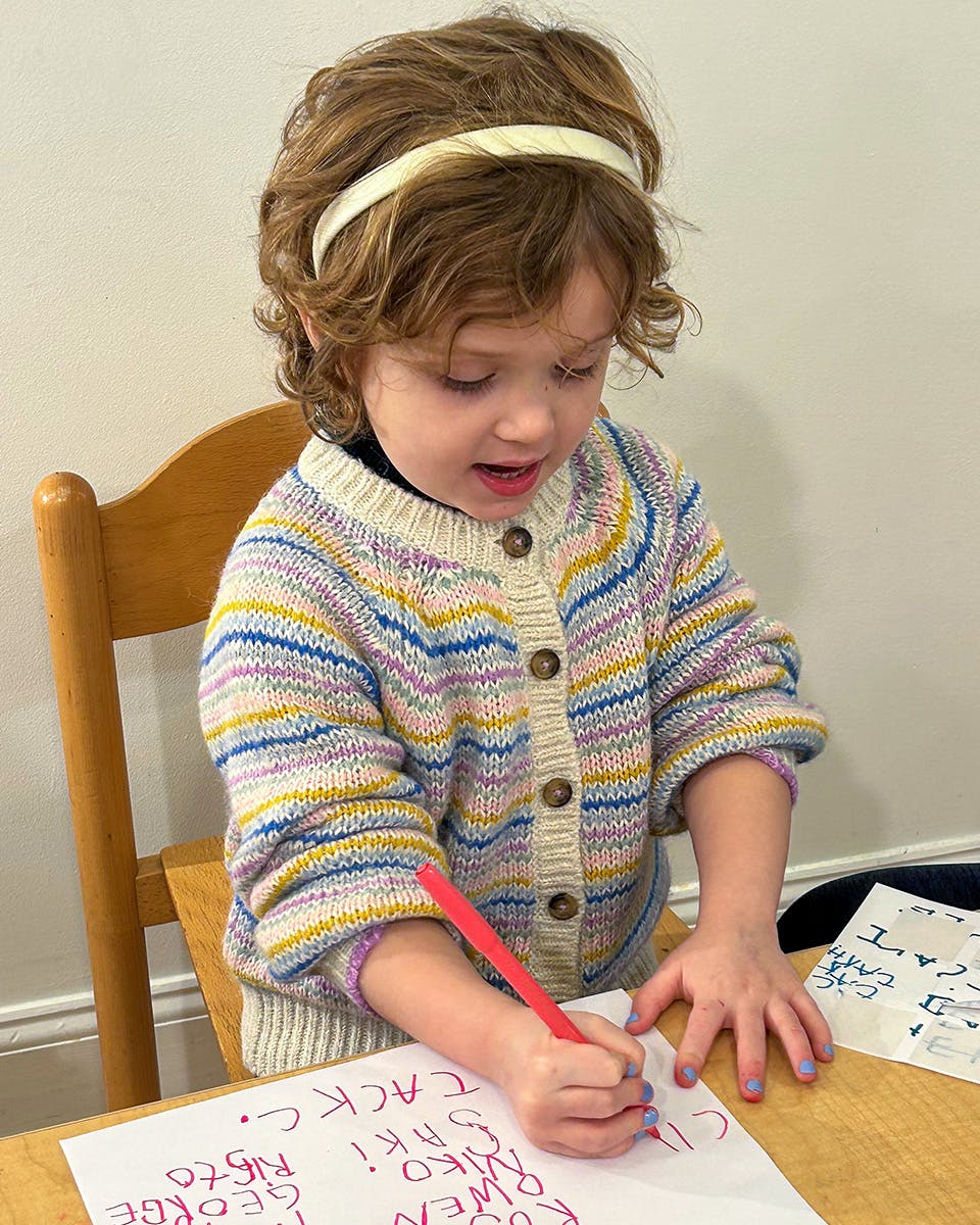 Child in a striped sweater writing on paper with a red marker