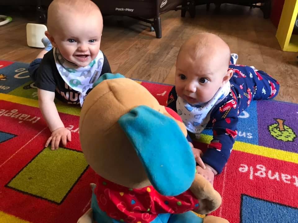 Two children on a colorful rug looking at a stuffed animal