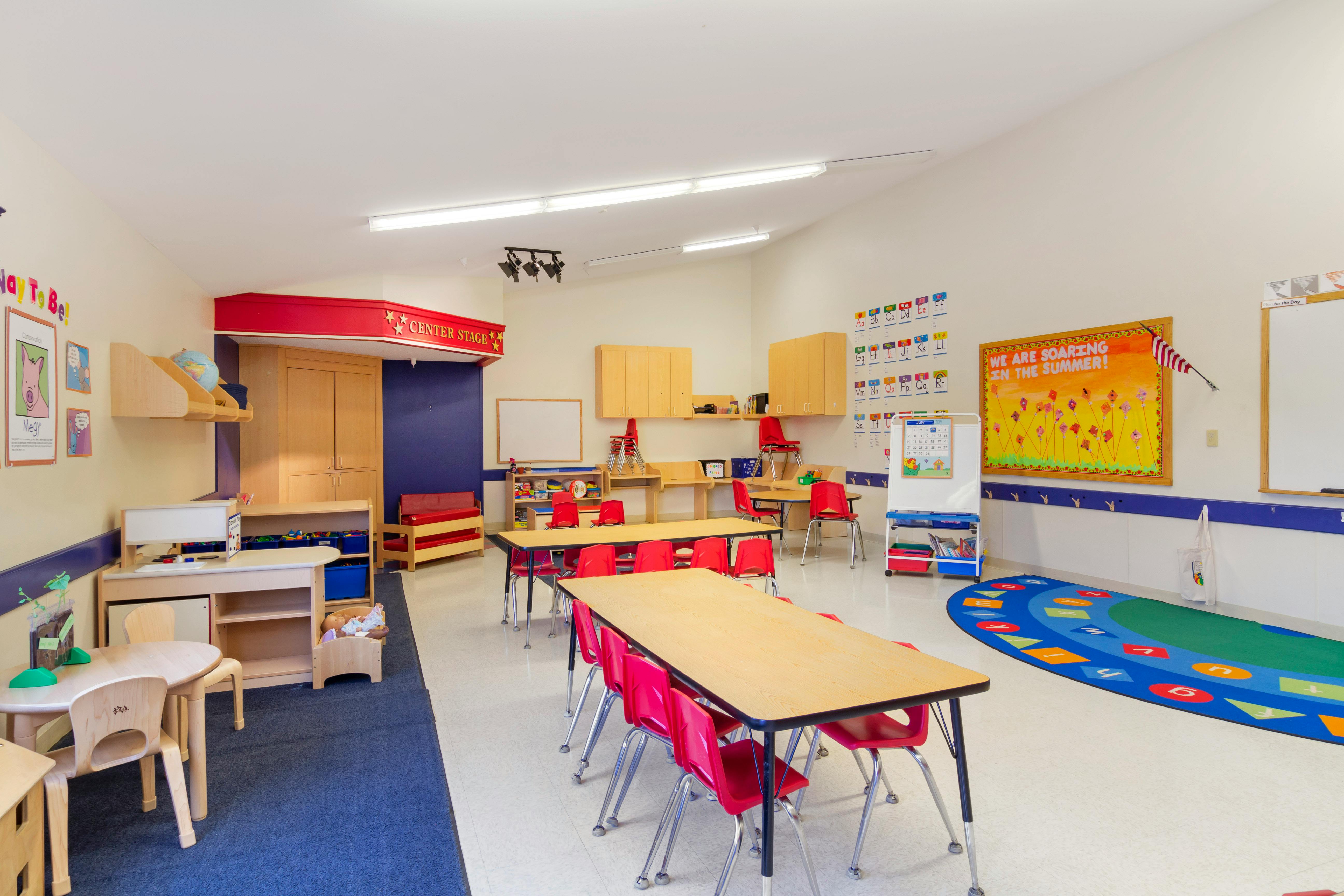 Classroom with child-sized tables and chairs, play area, and alphabet posters