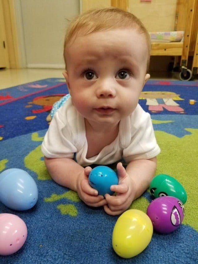 Child on floor holding a blue egg-green egg-shaped toy