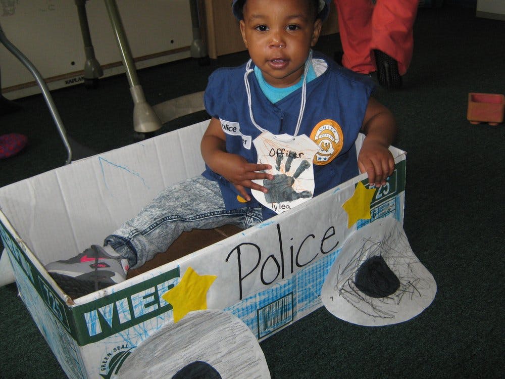 Child in a cardboard police car with "Police" written on the side