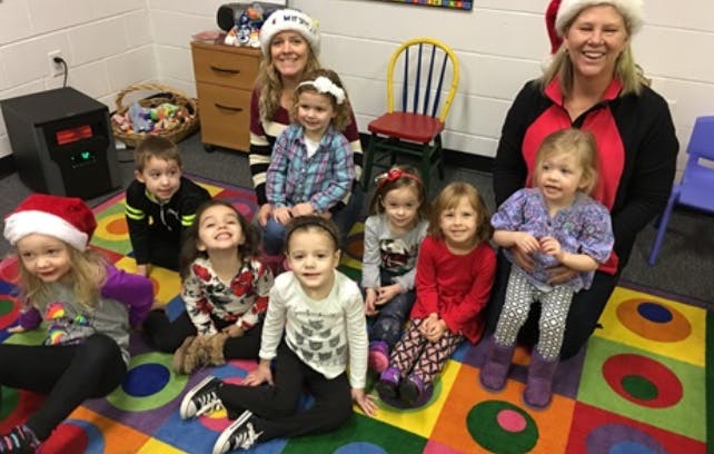 Two people and multiple children sitting on a colorful rug