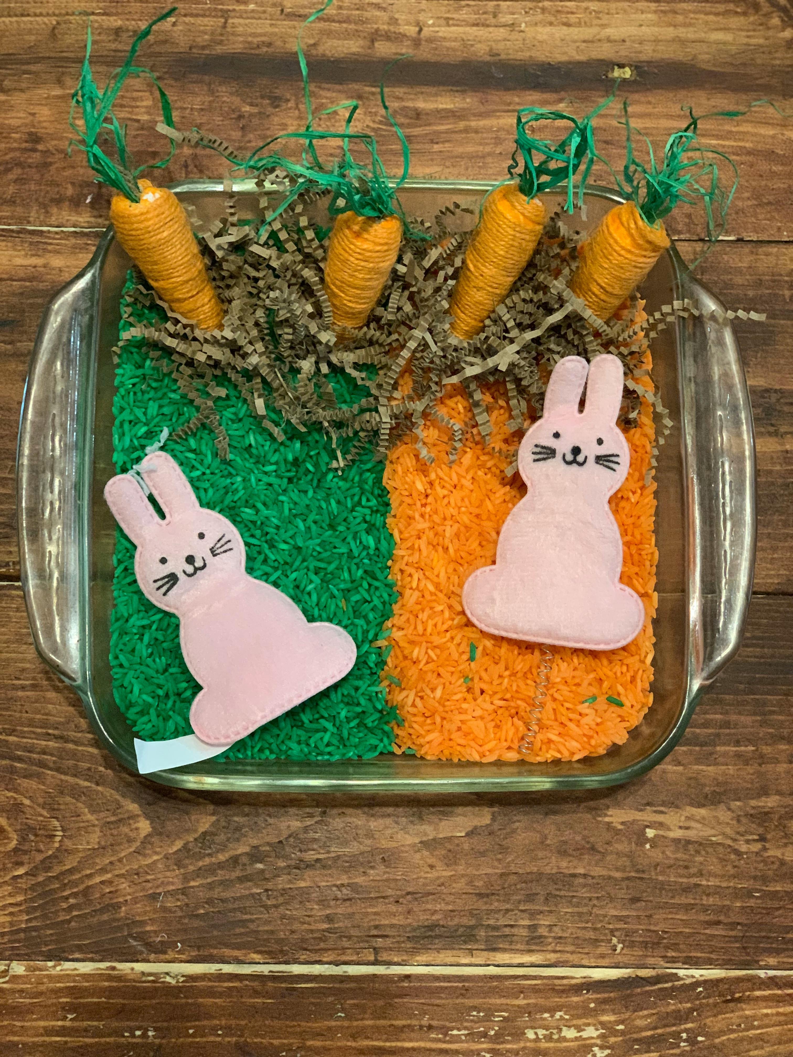 Two pink bunny cutouts and four carrot decorations in a glass dish