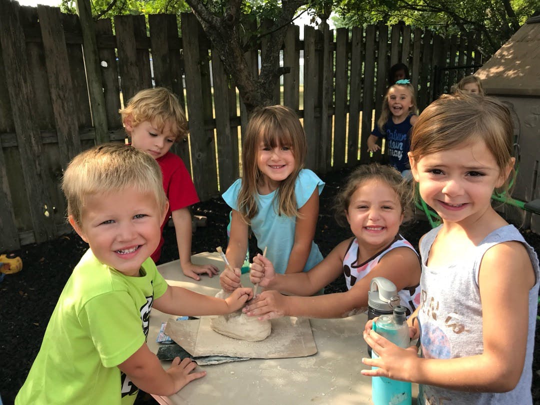 Children playing with clay at a table outdoors