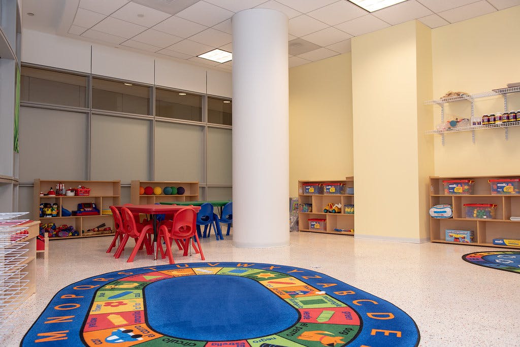Classroom with small red and blue tables and chairs, shelves, and alphabet rug