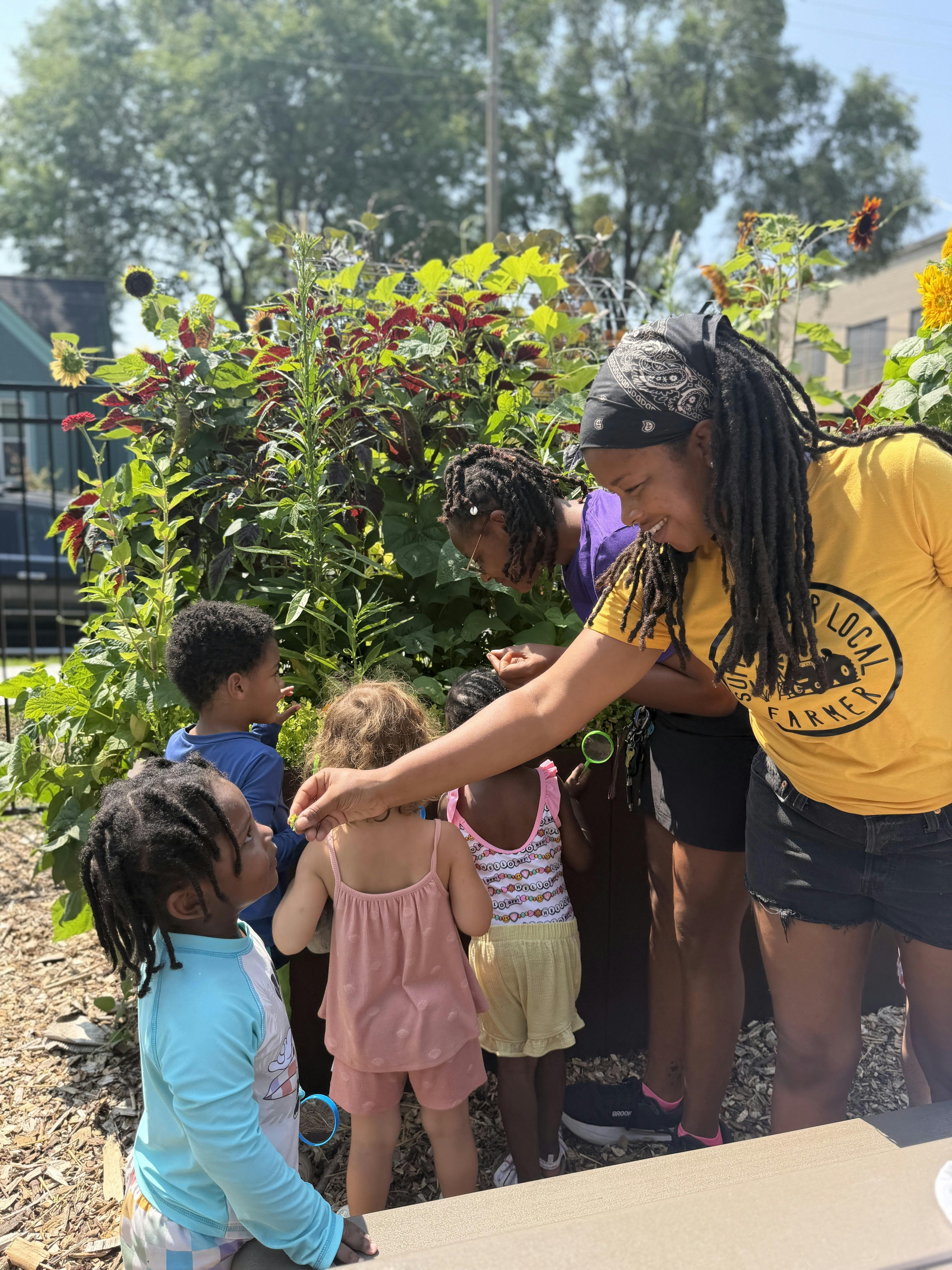 A person showing a plant leaf to a group of children in a garden