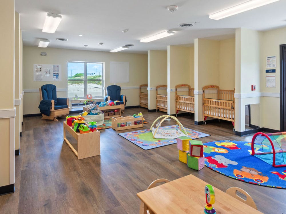 A brightly lit nursery room with cribs, play mats, and rocking chairs