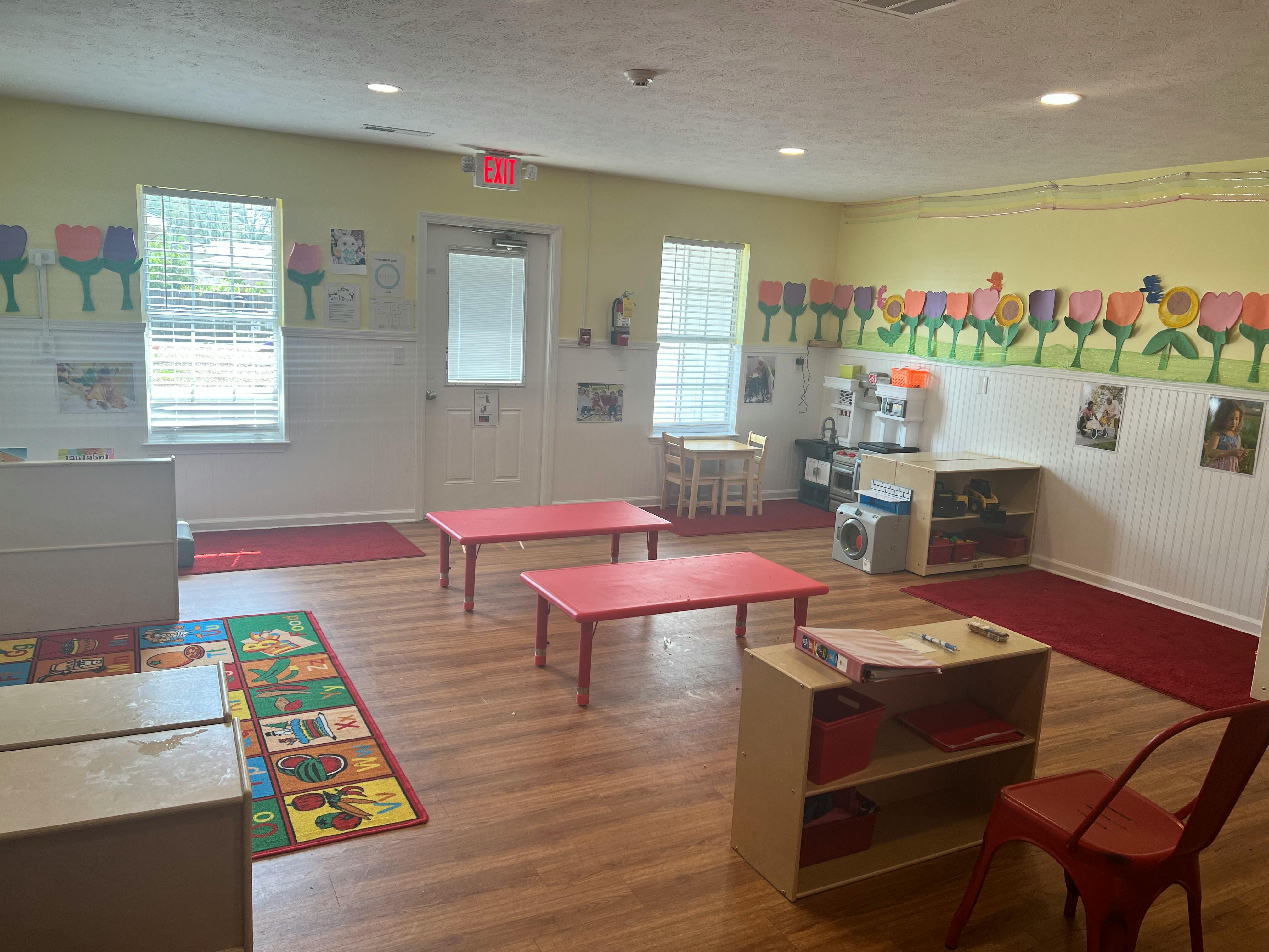 Classroom with small red tables and chairs, colorful rug, and wall decorations
