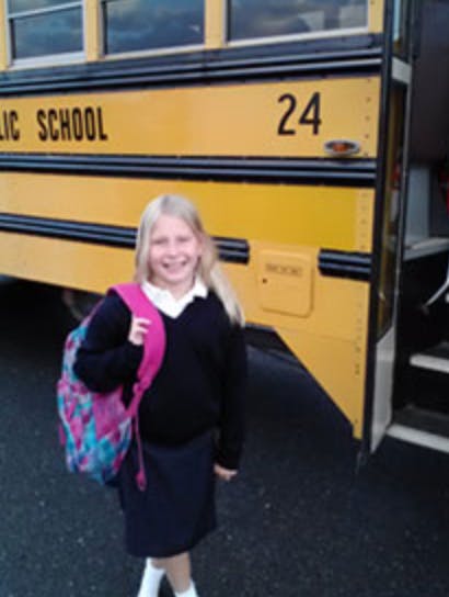 Child with a backpack standing in front of a school bus