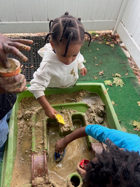 Child playing in a sand and water table with a yellow shovel