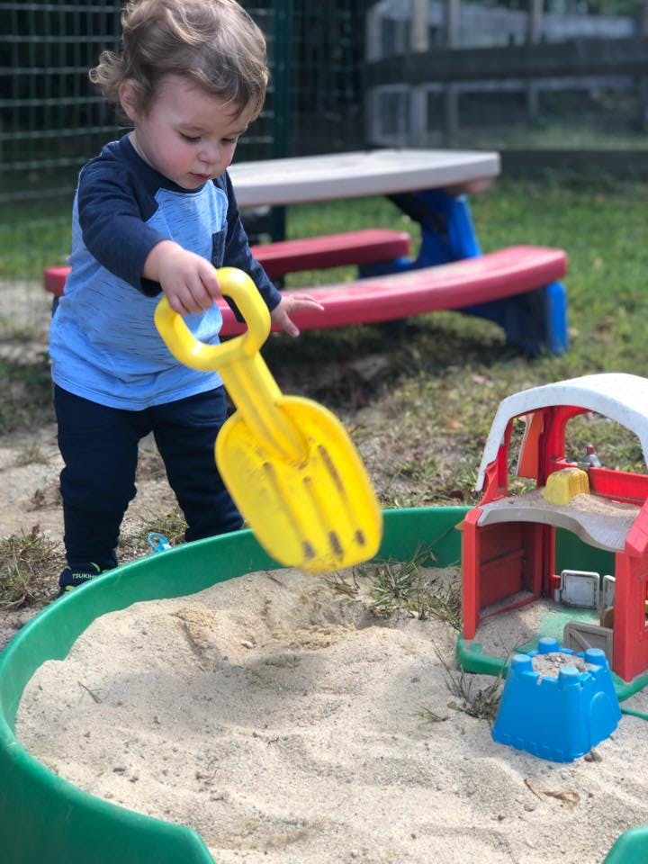 Child holding a yellow shovel over a sandbox