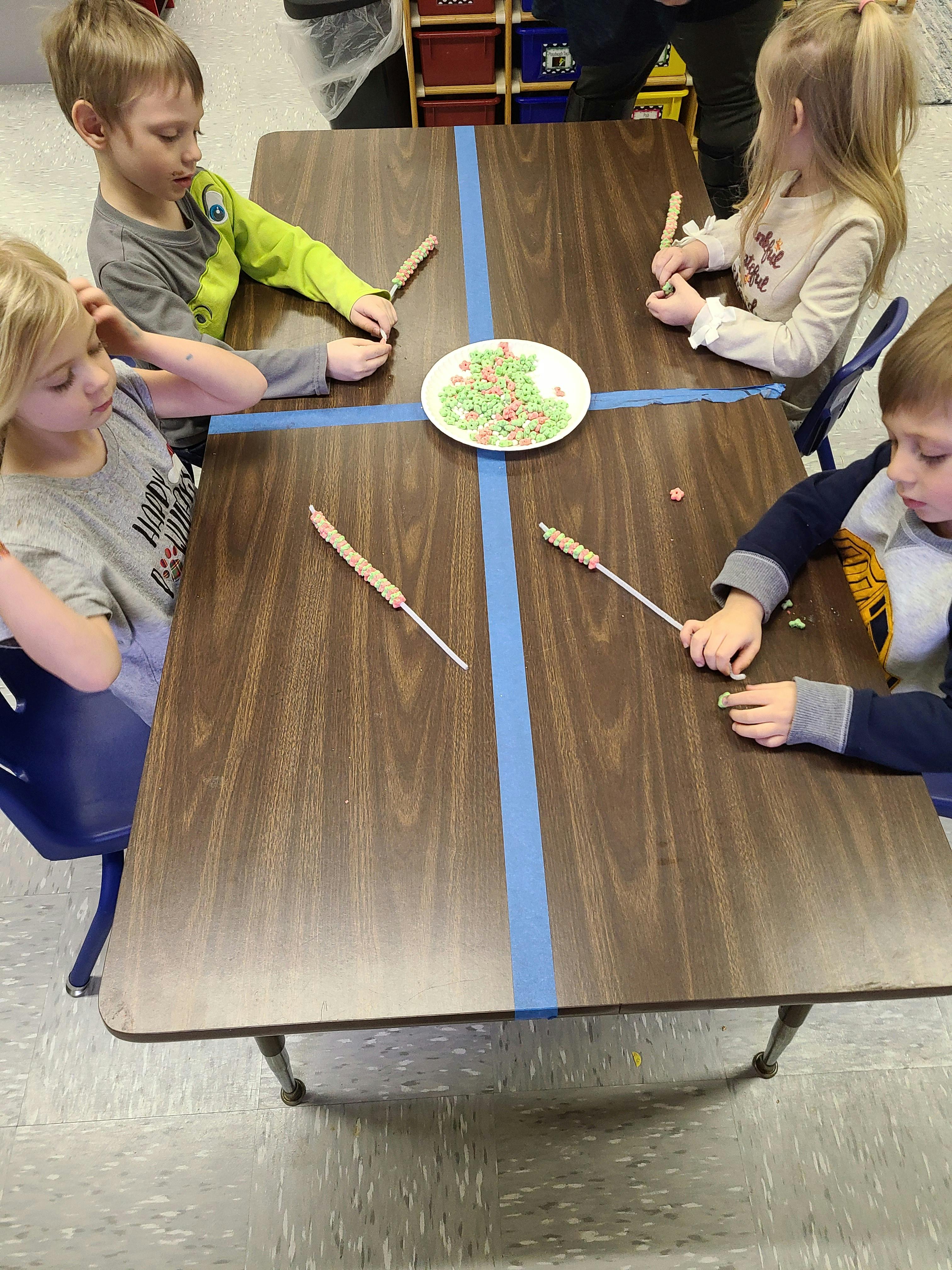 Four children decorating pretzel sticks with sprinkles at a table