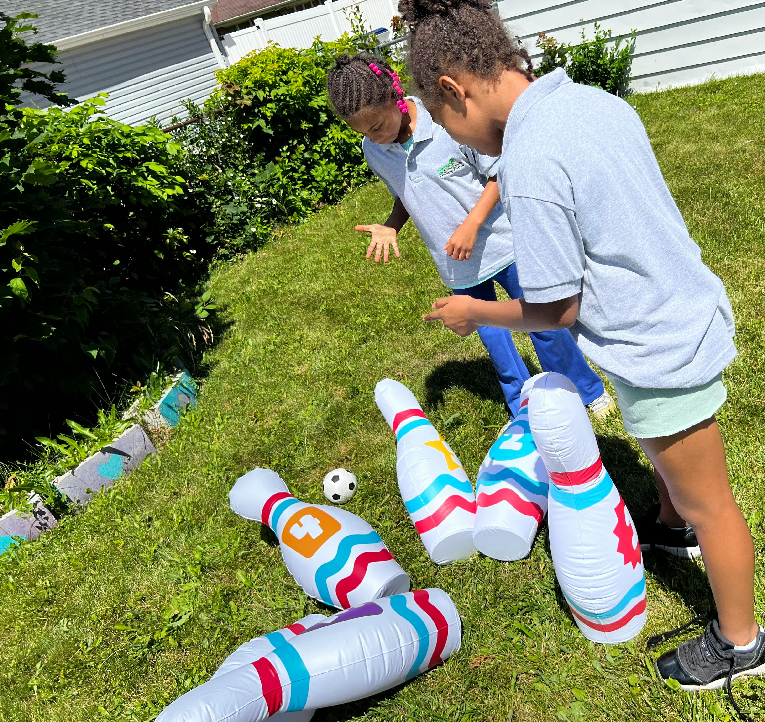 Two children playing with inflatable bowling pins and a small ball on grass