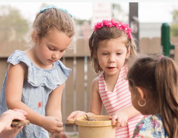 Three children playing with a bucket outdoors