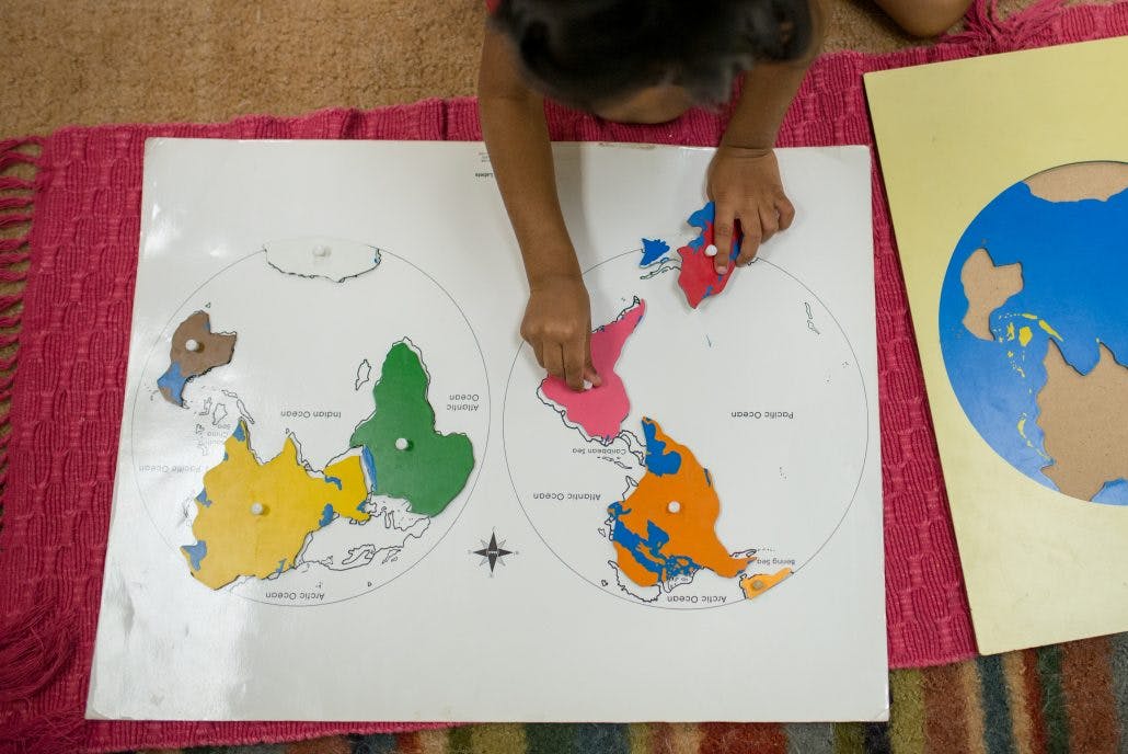 Child placing a puzzle piece of a continent onto a world map
