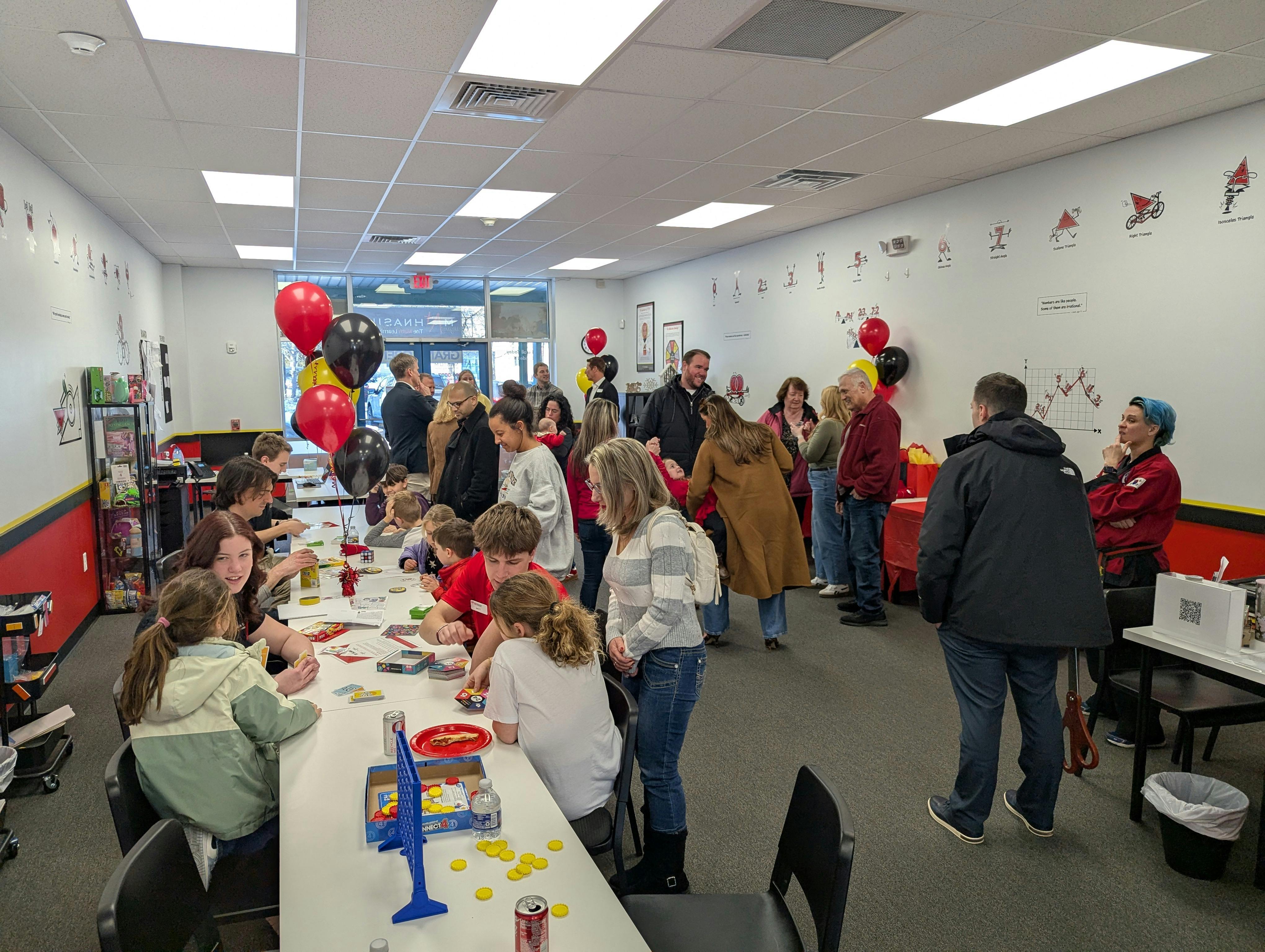 People gathered in a room with balloons, some playing board games at a table