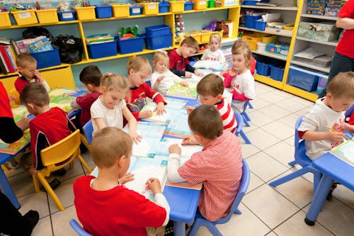 Children sitting at tables in a classroom, drawing and writing