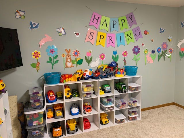 Wall decorated with "Happy Spring" banner and flower cutouts above toy shelves