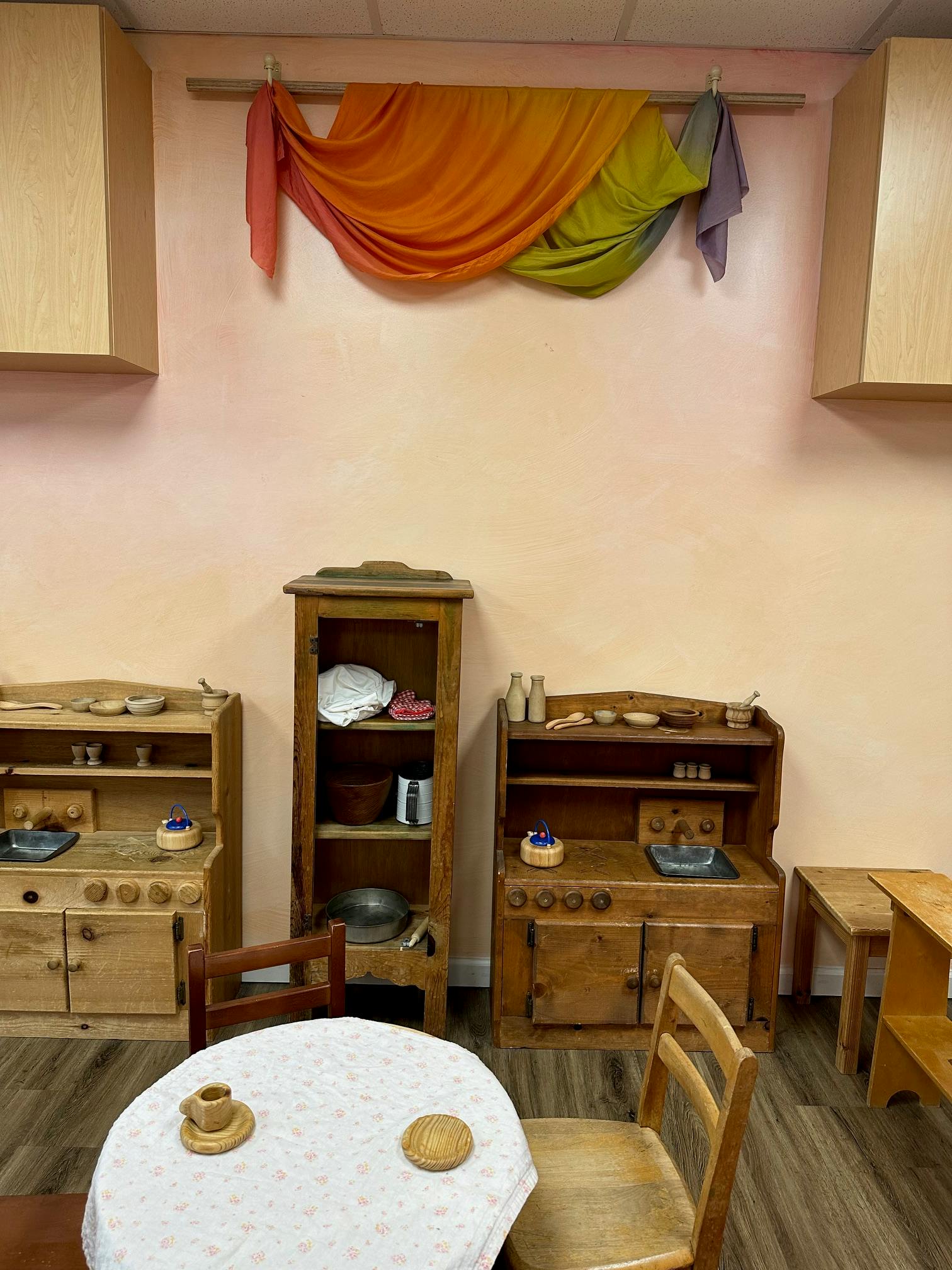 Play kitchen area with wooden furniture and a small table with chairs