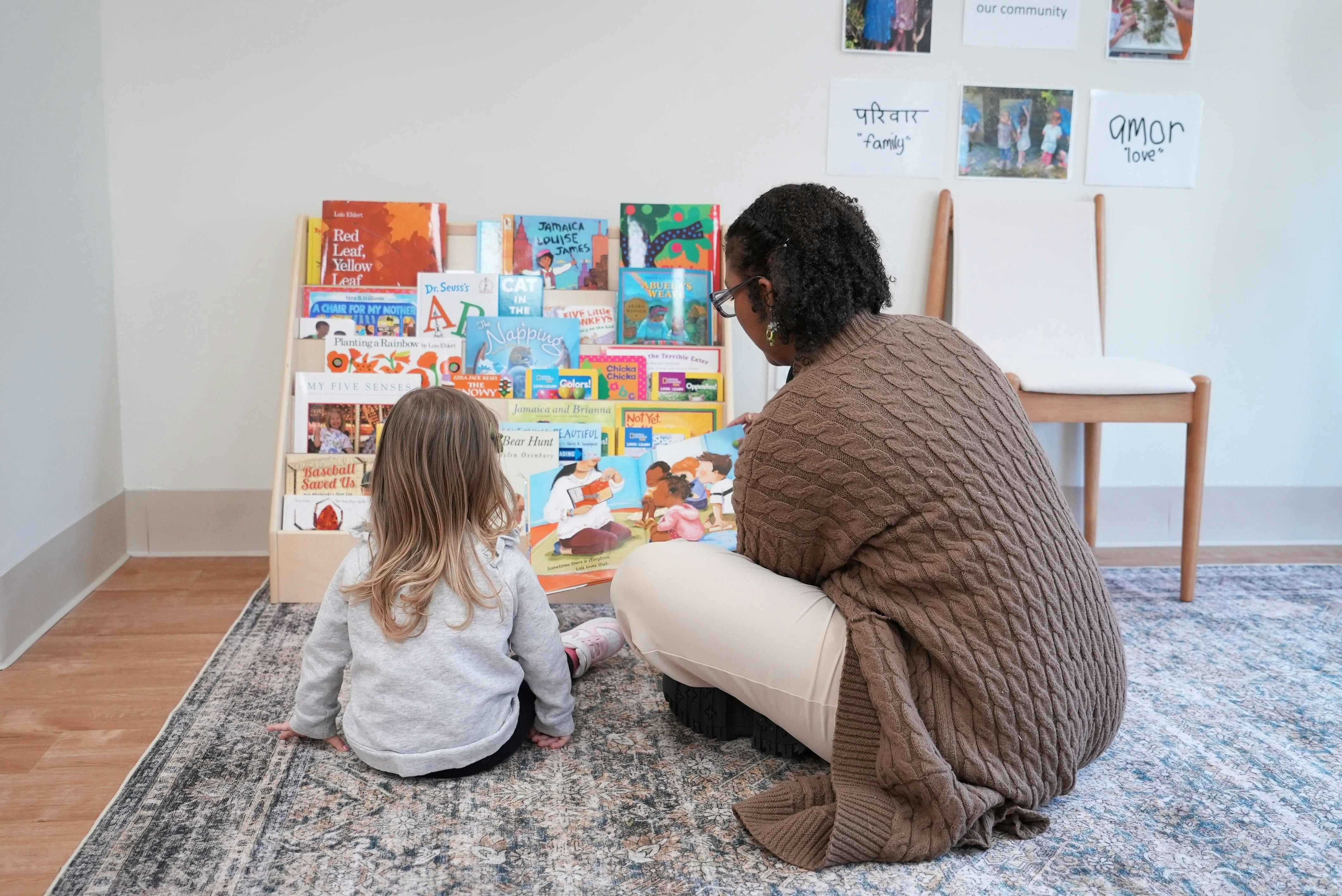 Adult and child sitting on a rug reading a book together in a classroom