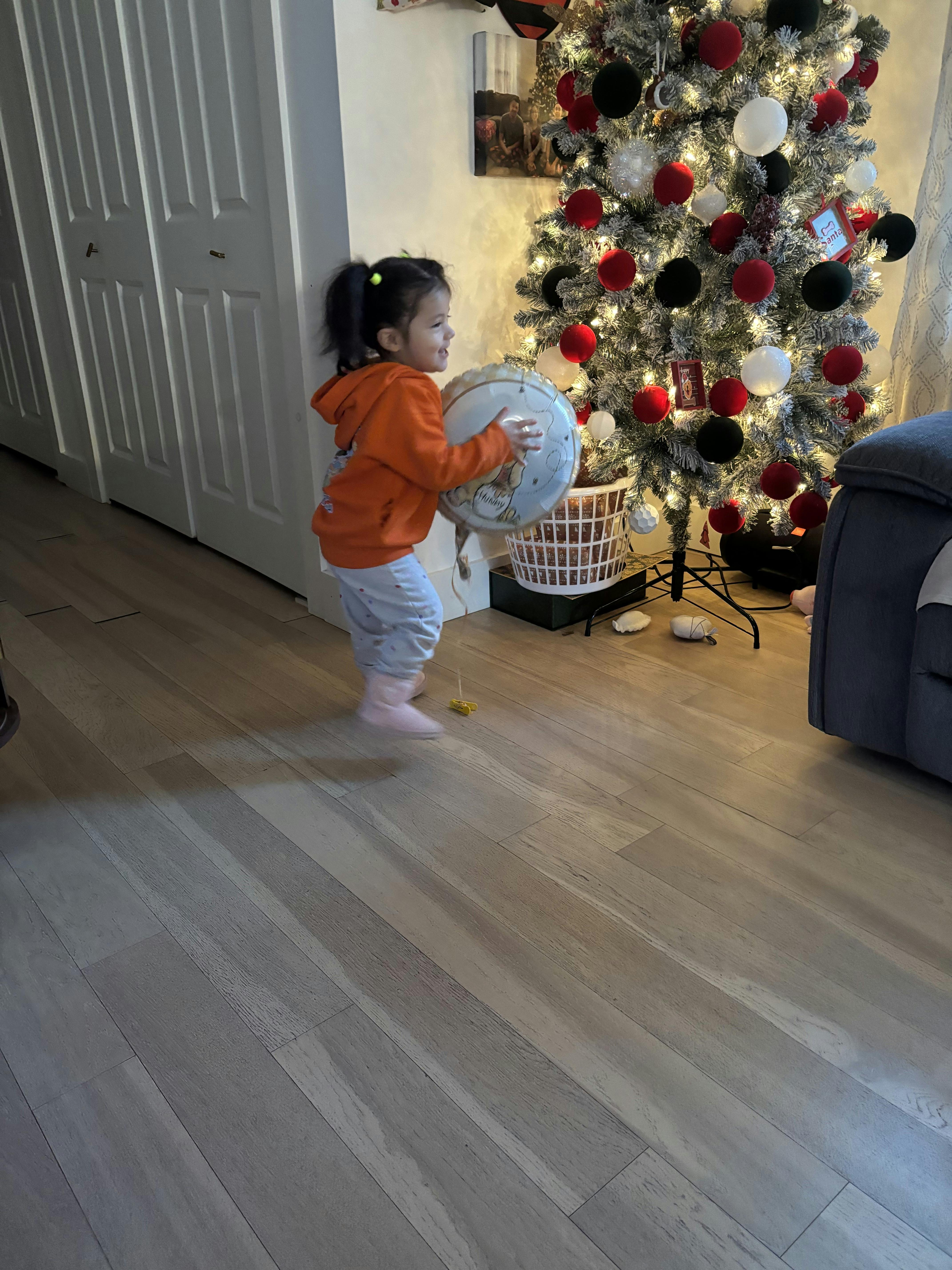 Child holding a balloon in front of a decorated Christmas tree