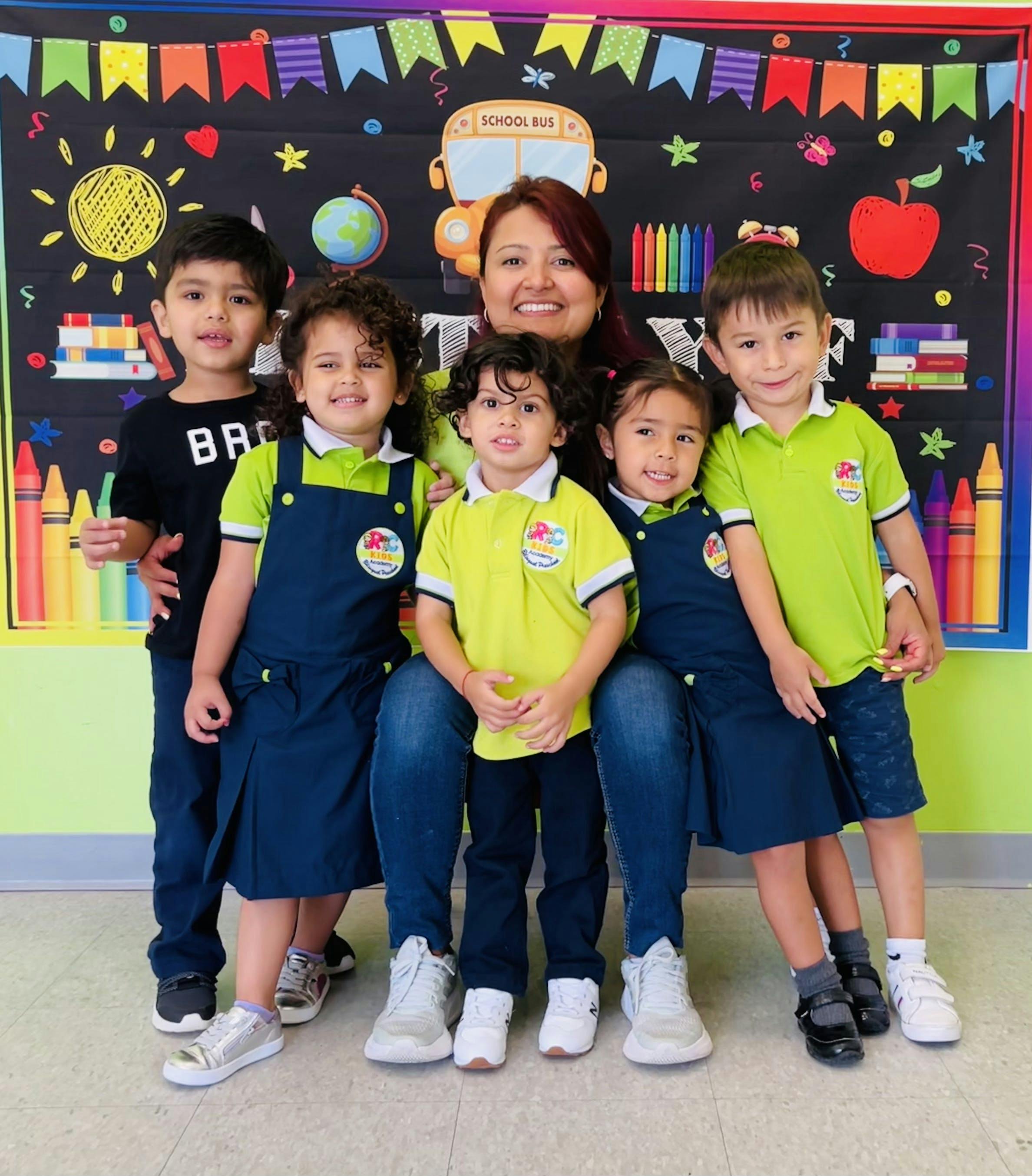 Adult and five children posing in front of a colorful classroom backdrop