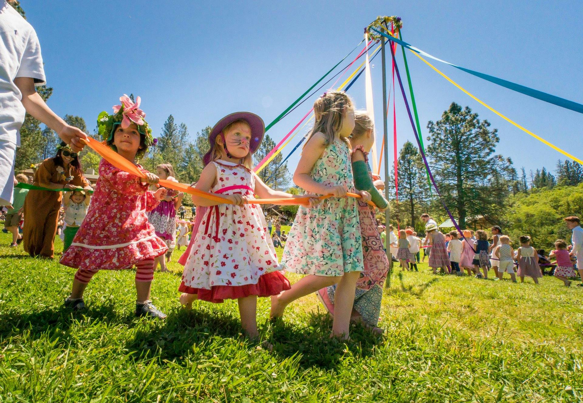 Children holding ribbons around a maypole on a sunny day
