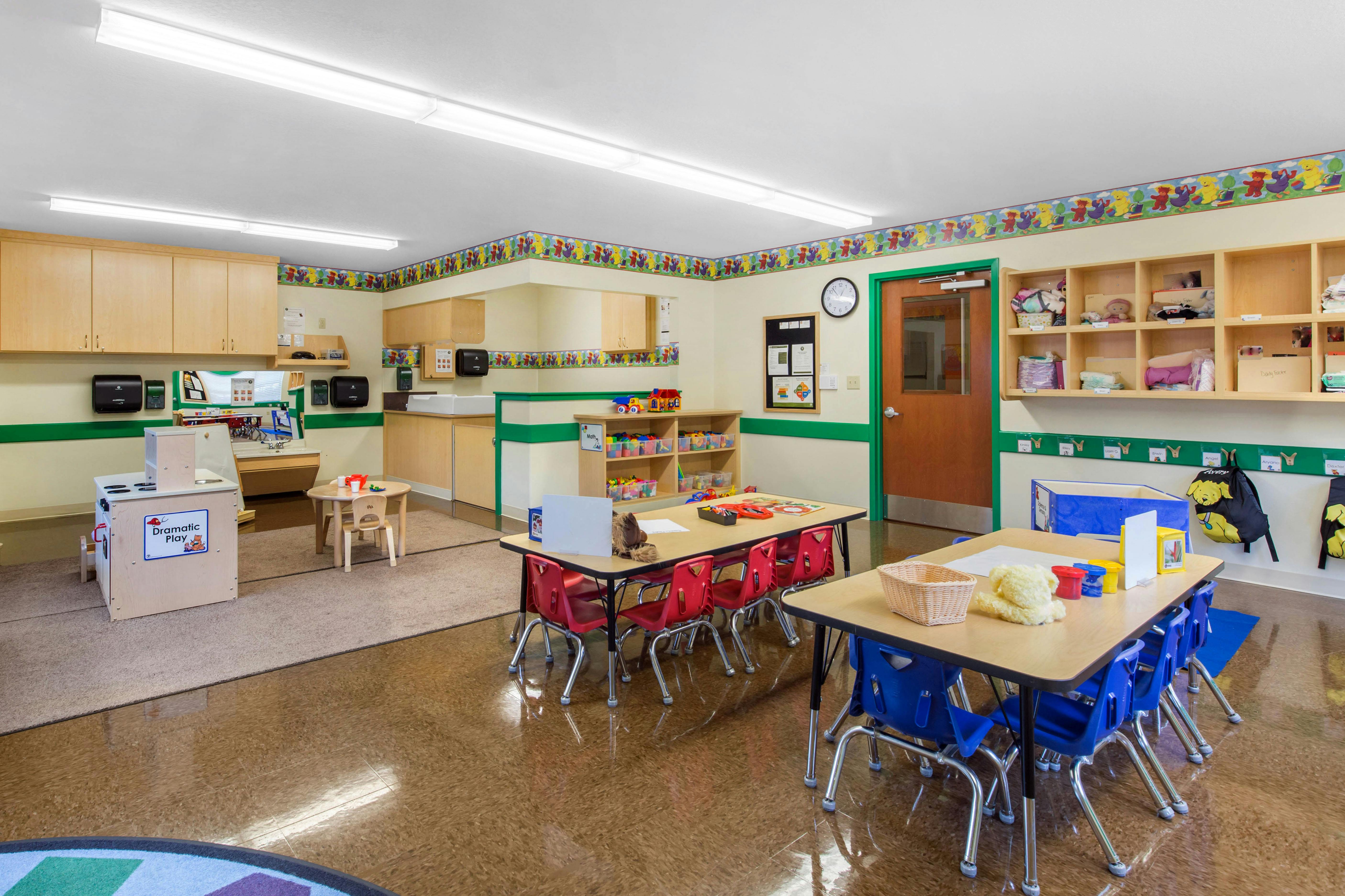 An empty childcare classroom with small tables and chairs