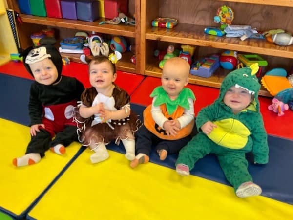Four babies in costumes sitting on a colorful floor