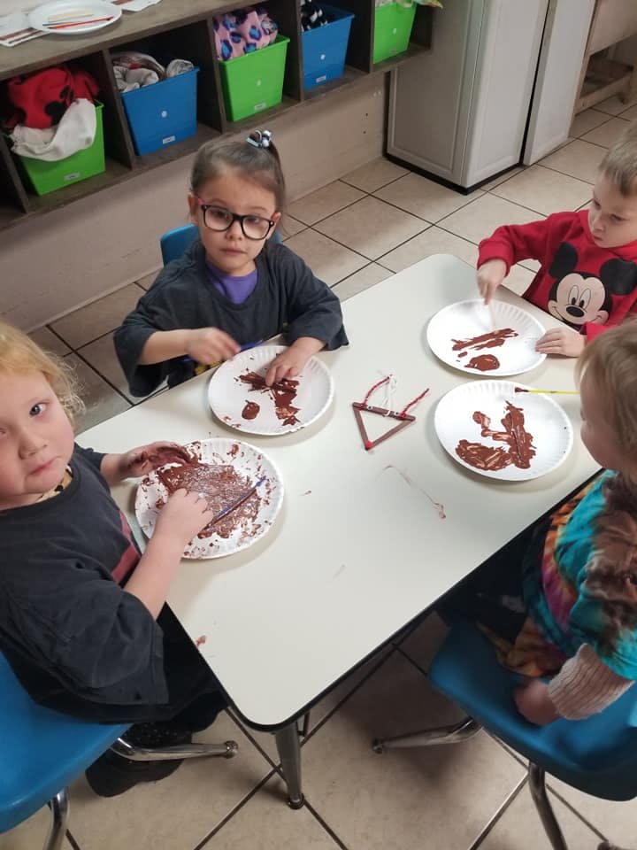 Children at a table with plates of brown paint