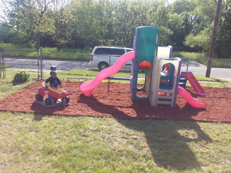 Child on a toy car next to a playground structure with slides