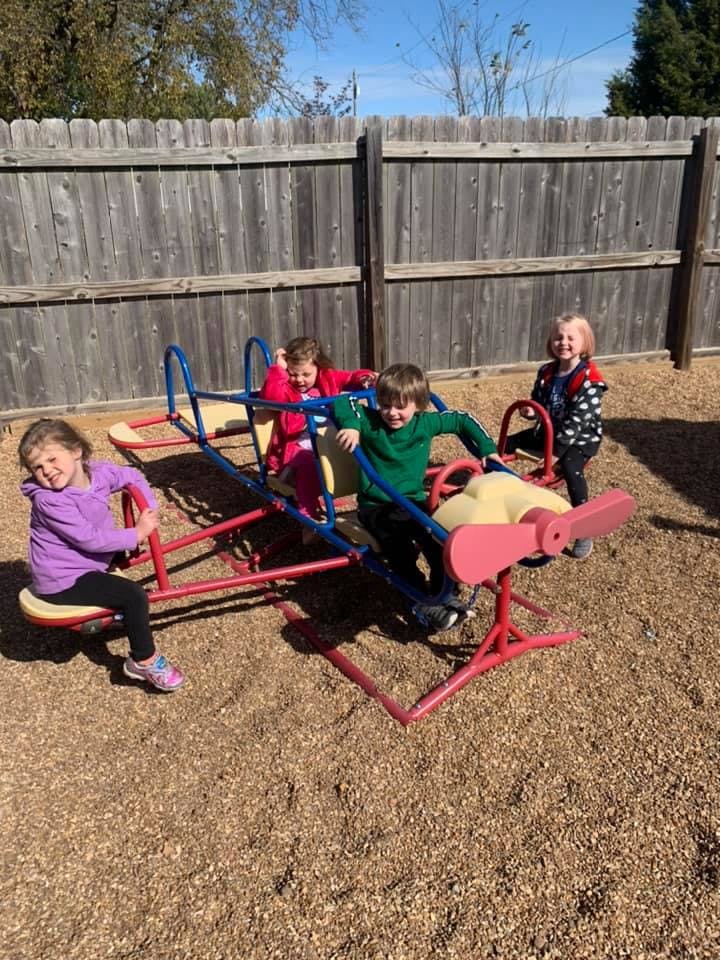Four children playing on a playground seesaw