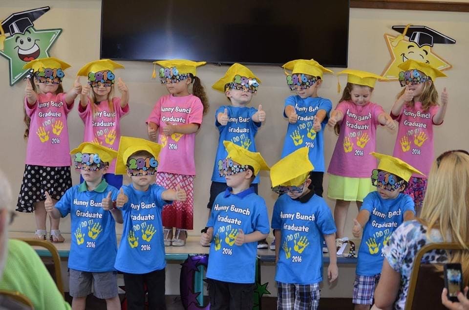 Children in graduation caps and novelty glasses standing on a stage