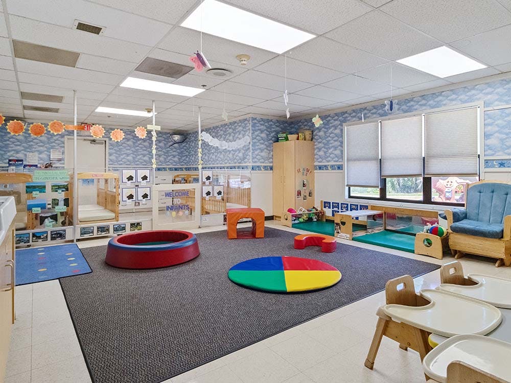 Classroom with cribs, play mats, and baby high chairs