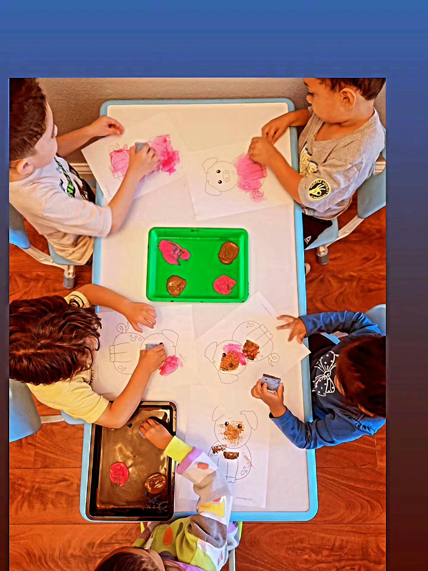 Children sitting at a table sponge painting pig outlines on paper